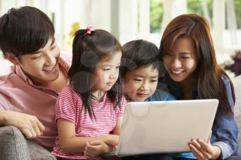 Chinese Family Using Laptop Whilst Relaxing On Sofa At Home