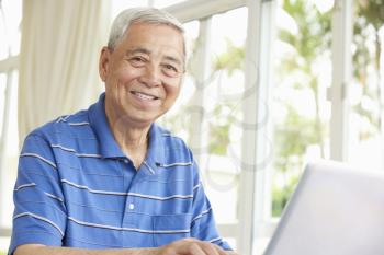 Senior Chinese Man Sitting At Desk Using Laptop At Home