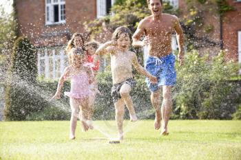 Family Running Through Garden Sprinkler