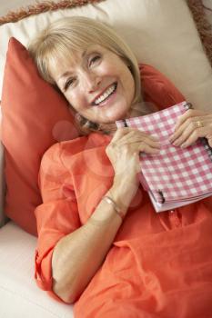 Senior Woman Sitting On Sofa Reading Diary