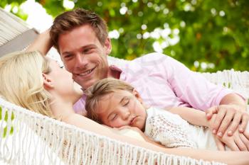 Family Relaxing In Beach Hammock With Sleeping Daughter