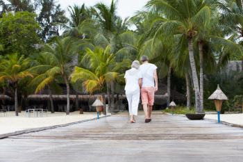 Rear View Of Senior Couple Walking On Wooden Jetty