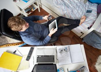 Teenage Boy Using Digital Tablet And Mobile Phone In Bedroom