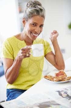Mature Woman Eating Breakfast And Reading Newspaper