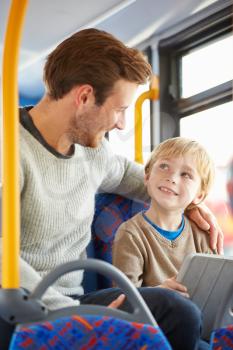 Son Using Digital Tablet On Bus Journey With Father