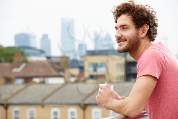 Young Man Relaxing On Roof Terrace With Cup Of Coffee