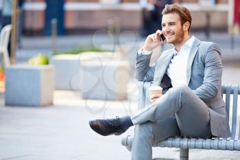 Businessman On Park Bench With Coffee Using Mobile Phone