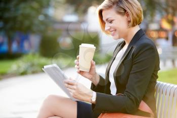 Businesswoman On Park Bench With Coffee Using Digital Tablet