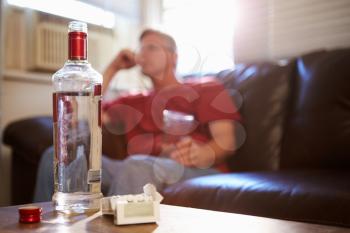 Man Sitting On Sofa With Bottle Of Vodka And Cigarettes