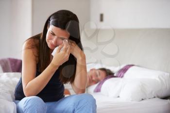 Woman Suffering From Depression Sitting On Bed And Crying