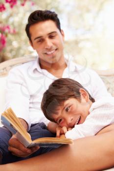 Father And Son Sitting In Garden Reading Book Together