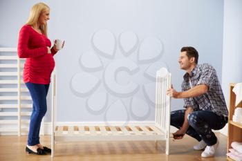 Couple With Pregnant Wife Assembling Cot In Nursery