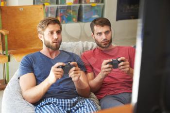 Two Male Friends In Pajamas Playing Video Game Together