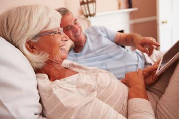 Senior Couple Lying In Bed Looking At Digital Tablet