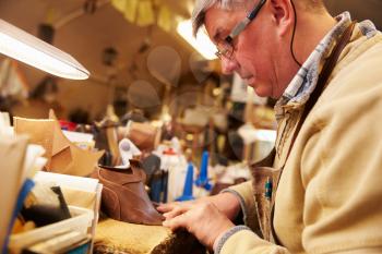 Senior shoemaker working with leather in a workshop, close up