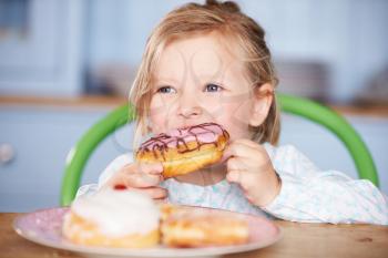 Young Girl Sitting At Table Eating Iced Donut