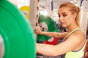 Woman preparing to lift barbells at a squat rack in a gym