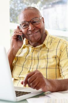 Senior Man On Phone Using Laptop At Home