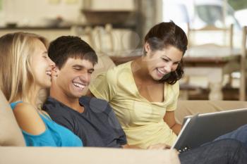 Three Teenagers  Sitting On Sofa At Home Using Tablet Computer And Laptop