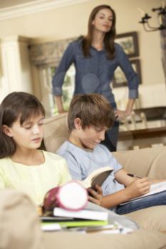 Two Children With Homework Sitting On Sofa At Home Whilst Mother Watches
