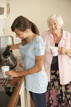 Teenage Granddaughter Sharing Cup Of Tea With Grandmother In Kitchen