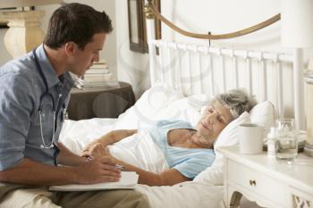 Doctor Talking With Senior Female Patient In Bed At Home