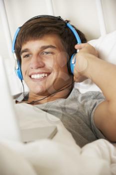 Teenage Boy Using Laptop And Headphones In Bed At Home