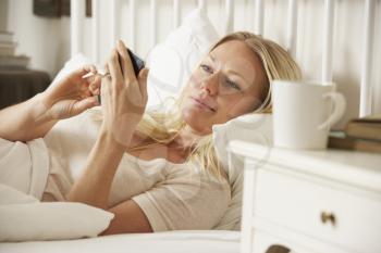 Woman In Bed At Home Texting On Mobile Phone