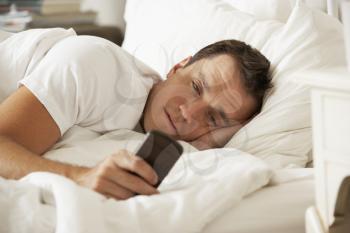Man In Bed At Home Texting On Mobile Phone