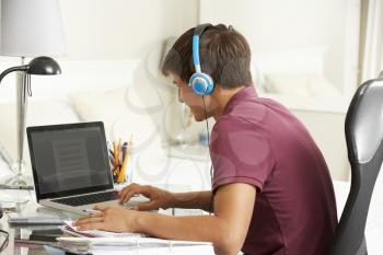 Teenage Boy Studying At Desk In Bedroom Wearing Headphones