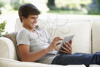 Teenage Boy Relaxing On Sofa At Home Using Digital Tablet