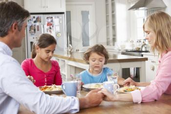 Family Praying Before Having Meal In Kitchen Together