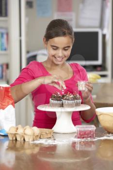 Girl Decorating Homemade Cupcakes In Kitchen