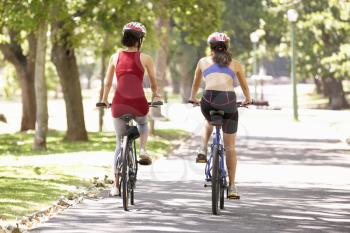 Rear View Of Two Women Cycling Through Park