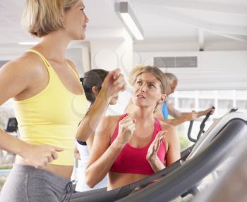 Woman On Running Machine In Gym Encouraged By Personal Trainer