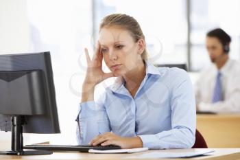 Stressed Businesswoman Working At Desk In Busy Office