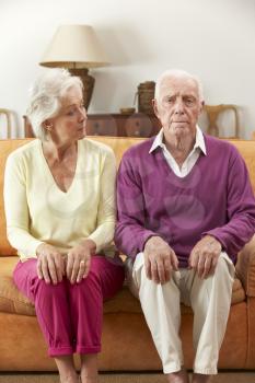 Serious Looking Senior Couple Sitting On Sofa At Home