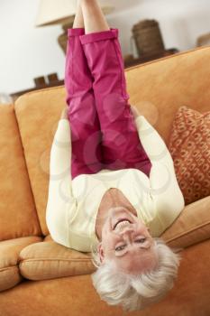 Senior Woman Lying Upside Down On Sofa At Home