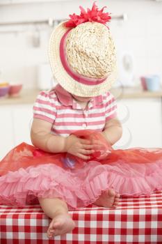 Little Girl Sitting On Kitchen Table Wearing Hat