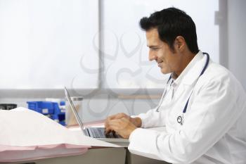 Male Doctor In Surgery Using Laptop