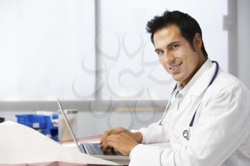 Male Doctor In Surgery Using Laptop