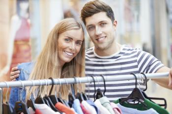 Couple Looking At Clothes On Rail In Shopping Mall