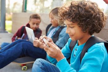Young Boys Using Digital Tablets And Mobile Phones In Park