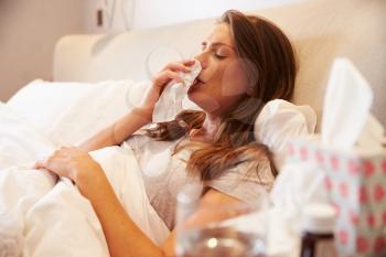 Woman Suffering From Cold Lying In Bed With Tissue