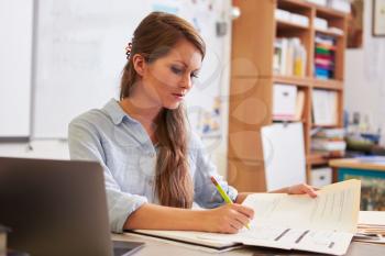 Young female teacher at her desk marking students� work