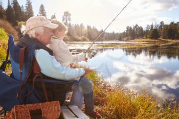 Senior man teaching his grandson to fish at a lake