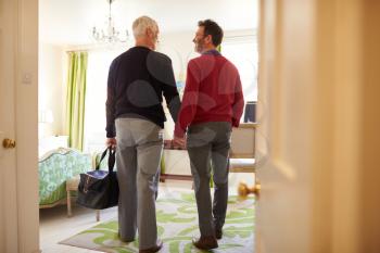 Middle aged male couple walk in to a hotel room, back view