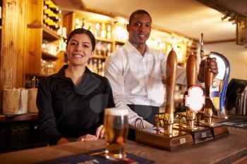 A young man and woman working behind a bar look to camera