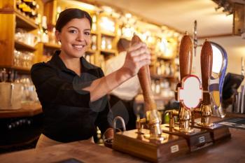 A young woman working behind a bar looking to camera, horizontal