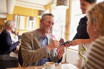 Senior couple paying waitress with card reader in restaurant